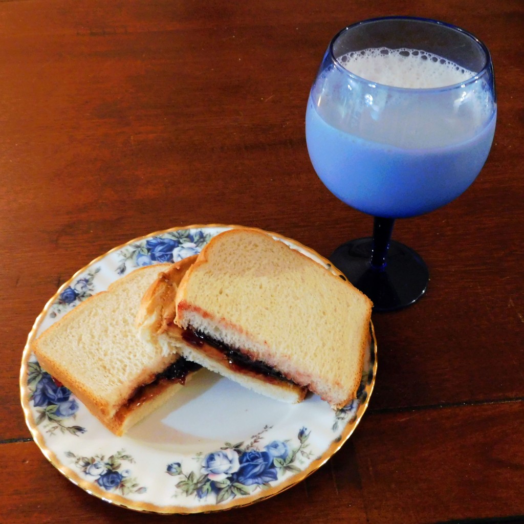 Peanut butter and jelly sandwich on fine gold and blue china; blue goblet of almond milk